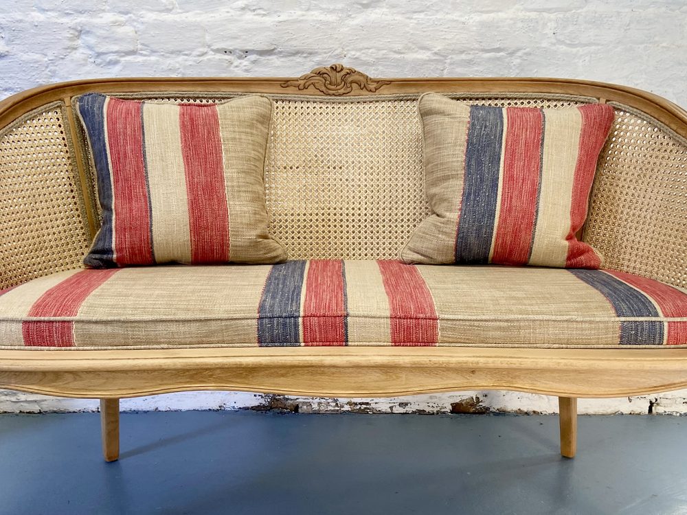 Dasselbe Sofa nach der Restaurierung: helles Holz, neues Geflecht und Polster mit rot-blau gestreiftem Stoff